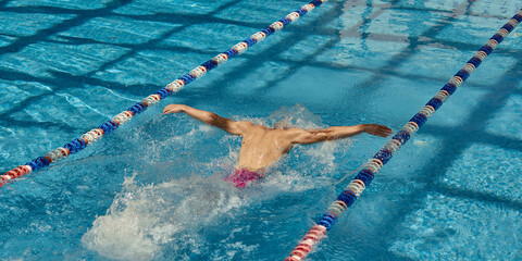 A competitive swimmer practices the butterfly stroke in clear blue swimming pool lanes, showcasing strength and form. Concept of athletic dedication and aquatic prowess.