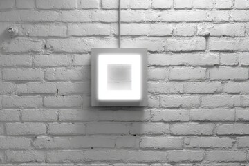 A square, light-emitting frame on a white brick wall