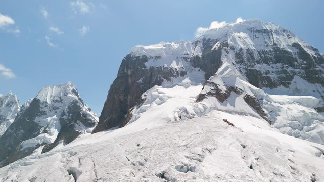 Stunning aerial pan left reveals the snow-laden Trapecio Pass amidst rugged alpine peaks and glaciers on the wild Cordillera Huayhuash trekking route in Peru.