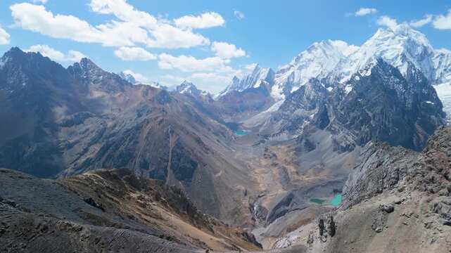 Epic aerial pull back shot from San Antonio Pass reveals panoramic snow-capped peaks, turquoise glacial lakes, and vast wild valleys of the Cordillera Huayhuash in Peru.