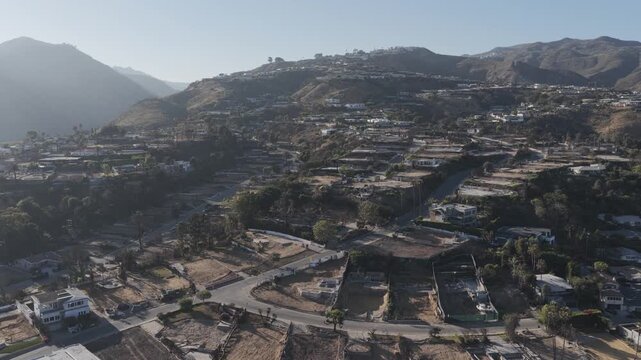 Aerial drone footage flying over the hills of Pacific Palisades, California, showing charred land, damaged homes, and active rebuilding after recent wildfires impacted the residential area.
