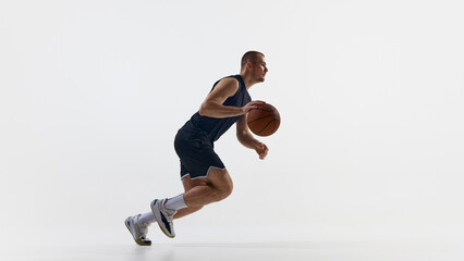 Athlete dribbling basketball in motion against plain background. Concept of acceleration,...