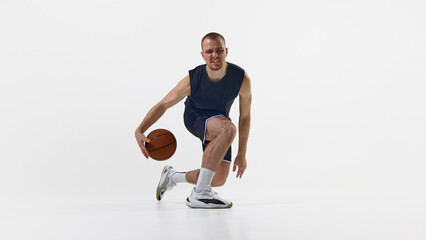 Basketball player dribbling low with determined face on white background in athletic crouch...