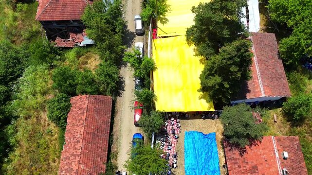 Aerial view of keşkek day and rain prayer ceremony in kurtlu village schoolyard, located near boyabat in sinop province, showing villagers gathered under tents with turkish flags and nature Turkiye 4k