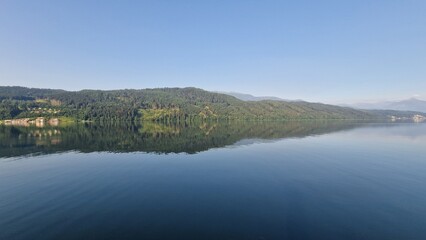 Serene mountain lake with greenish water, mirror-like reflections, forest and sky blending in nature’s harmony