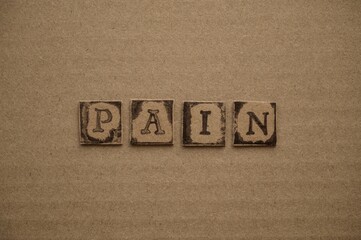 Word Pain spelled out from cardboard letters made by black alphabet stamps on a cardboard background