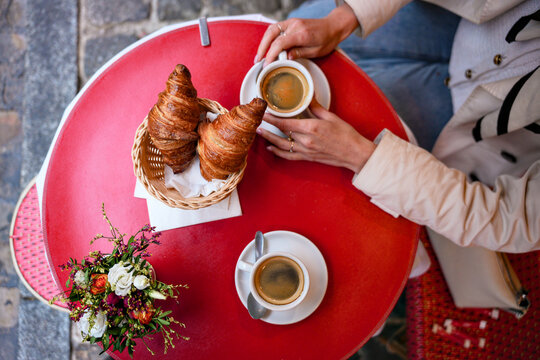 Overhead shot of two people enjoying croissants and coffee at outdoor cafe table