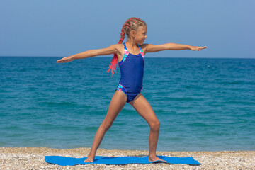 A child doing Warrior 2 Pose as a fun beach yoga concept by the seaside
