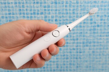 Electric toothbrush in hand against a blue tiled background during morning routine for effective dental care