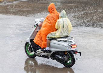 A person with a girl in school uniform ride in the rain on a motorcycle, Thailand