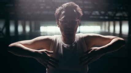 Zoom in slowmo of young Caucasian man wearing eyeglasses dancing in dark warehouse building, looking at camera