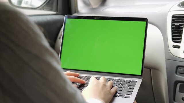 Person is typing on a laptop with a green screen. The laptop is on a car