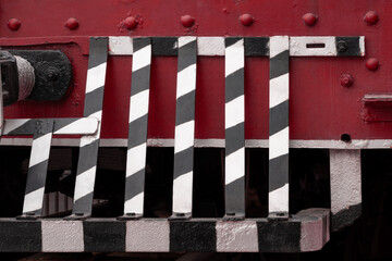 Vintage steam locomotive grill guard with weathered metal surface, rivets and colorful paint patches. Industrial railway heritage detail showing authentic wear, patina on antique train equipment.