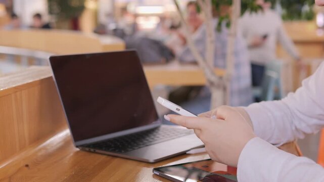 Woman is sitting at a table with a laptop and a cell phone. She is holding the cell phone in her hand