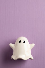 A Simple and Cute White Ceramic Ghost Figurine on a Light Purple Textured Background, with Ample Vertical Copy Space for Minimalist Halloween Designs
