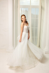 Fototapeta premium Beautiful bride twirls in elegant gown against a bright window backdrop