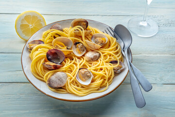 Vongole clams with spaghetti pasta, with lemon, with a wine glass, on a rustic wooden table