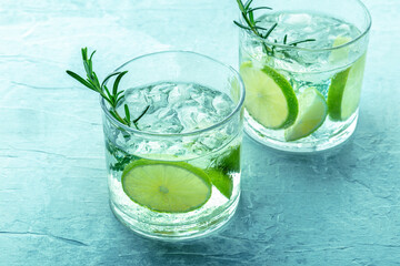 Gin tonic, two glasses of gin with soda, lime, rosemary, and ice, on a blue background, fresh summer drinks