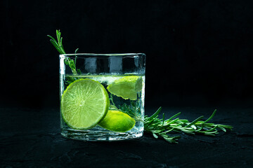 Gin tonic, a glass of gin with soda, lime, rosemary, and ice, side view on a black background, with a place for text