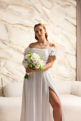 Bride wearing elegant white dress poses with bouquet in modern setting during wedding preparation