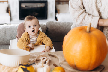 Happy mother and cute baby son with funny emotion with pumpkin on table. Family carving halloween...