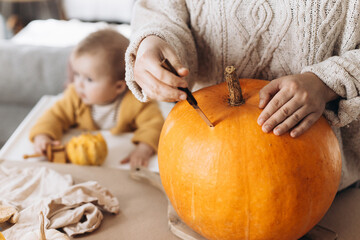 Happy Halloween. Happy mother carving halloween pumpkin together with baby son on table with spooky...