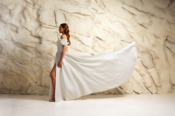 Elegant woman in flowing white dress poses gracefully against textured backdrop
