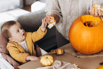 Family carving halloween pumpkin. Happy mother and cute baby son cutting pumpkin on table with...