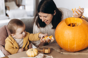 Happy mother and cute baby son carving pumpkin on table with ghosts, spiders and bats decoration....