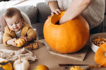 Happy mother and cute baby son carving pumpkin on table with ghosts, spiders and bats decoration....