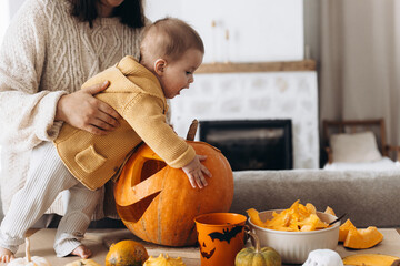 Happy mother and cute baby son carving pumpkin on table with ghosts, spiders and bats decoration....