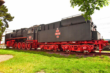 Locomotora de vapor expuesta al aire libre, frente a edificio ferroviario clásico.Teius ,Romania