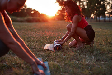 Two women folding and unfolding yoga mat in the park during sunset sunrise time.