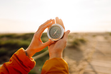 Close-up of a young female traveler's hands holding a compass against the backdrop of a sunset...