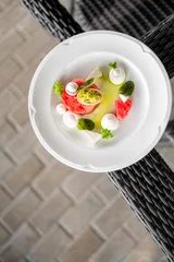 Gordijnen Gourmet appetizer with watermelon slice topped with avocado, herbs, and cream, elegantly plated on white dish in a stylish restaurant setting. © pavel siamionov