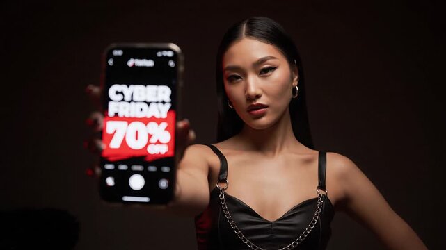 Fashion blogger woman of Asian appearance shows the screen of her smartphone to the camera. The phone shows inscriptions about sales and big discounts and sales.