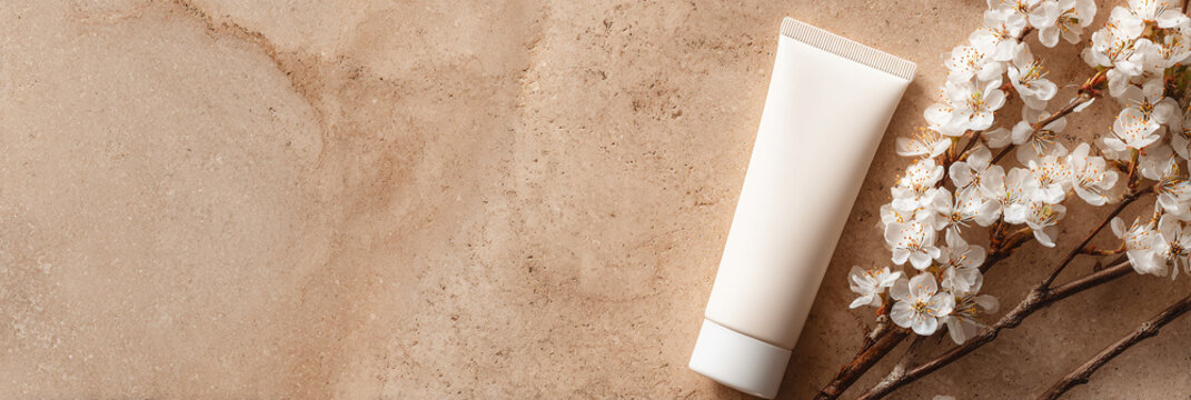 Tubo di crema cosmetica bianca su sfondo legno chiaro con fiori bianchi
