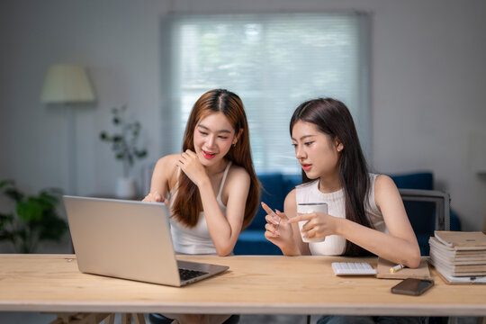 Two women are sitting at a table with a laptop and a cup of coffee