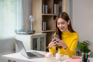 A woman in a yellow sweater is sitting at a desk with a laptop and a cell phone