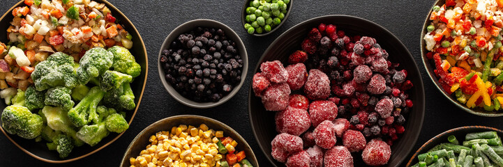 Frozen summer vegetables and fruits in plates, set on a dark background, emphasizing the seasonal...