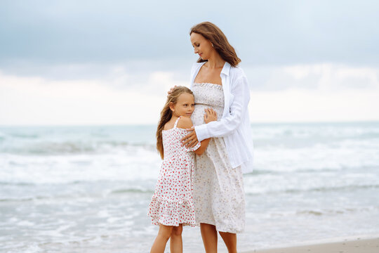 Young pregnant mother with daughter walking on sandy beach. Happy woman with child having fun and enjoying time together. Childhood, pregnancy and nature concept.