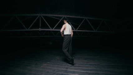 Young Caucasian male contemporary dancer wearing eyeglasses performing in dark warehouse space