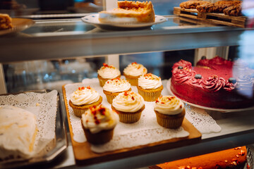 Fresh and flavorful desserts are tempting under the glass dome of this cozy bakery. Cozy atmosphere with fragrant cinnamon buns, cupcakes and muffins in the coffee shop. Dessert and food concept.