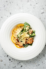 Colorful healthy meal with grilled squash, chicken, couscous, spinach, and cherry tomatoes served on a white plate over a speckled countertop, top view.