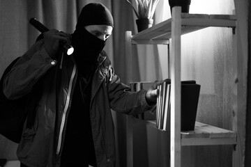 Thief in black balaclava. Robber with flashlight entering a house for stealing at night. Copy space
