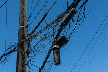 A power pole with a tangle of wires and cables against a blue sky. Industry, structure.