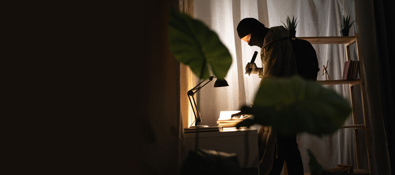 Burglar or intruder with flashlight. Illegally breaking. Male robber wearing black balaclava steals money from apartment. Thief committing theft. Criminal offence. burglary and housebreaking