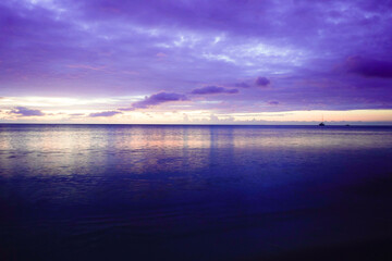 A wide ocean, pastel-colored skies with soft clouds, and calm waters create a dreamy sunrise...