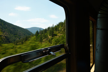 Fototapeta premium Scenic view through an open train window in Mokra Gora, Serbia, with forested hills and blue sky.