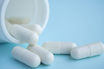 medicine pills capsule spilling out of bottle on blue background